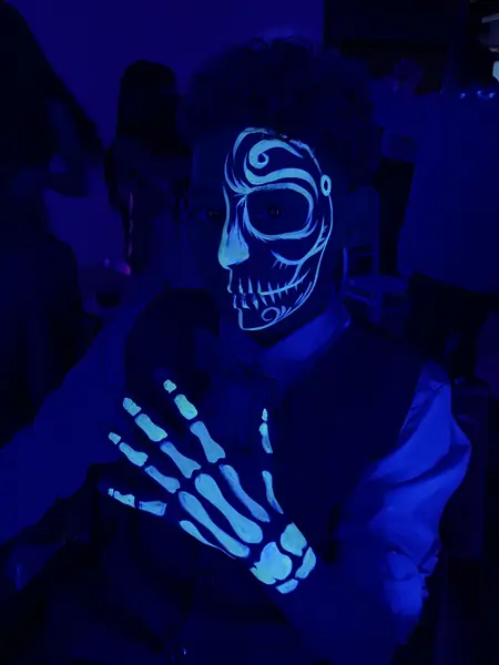 Maquillaje flúor de calavera en el rostro y huesos en la mano de un hombre