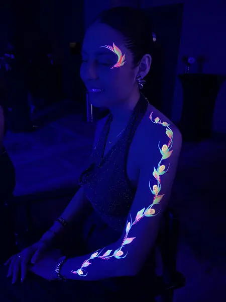 Maquillaje flúor de enredadera en el brazo y flor en el ojo de una mujer