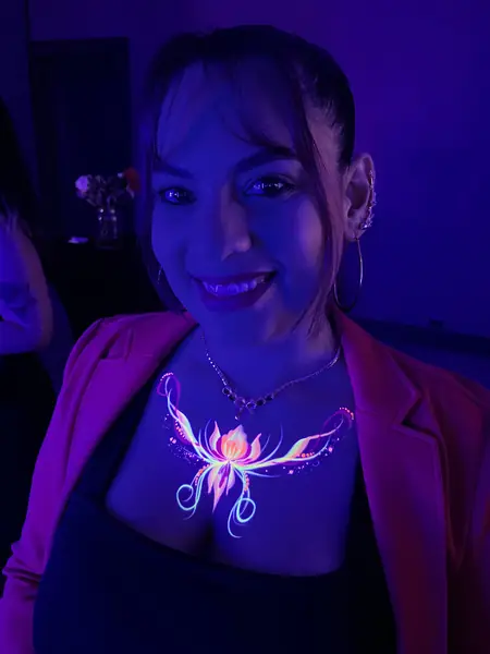 Maquillaje flúor de flor en el escote de una mujer, brillando con luz ultravioleta