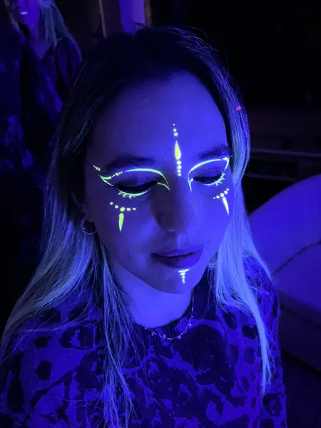 Maquillaje flúor de líneas y puntos en el rostro de una mujer bajo luz UV