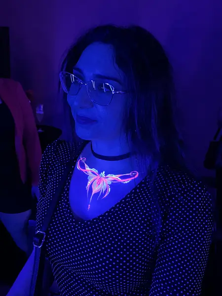 Maquillaje flúor de mariposa en el escote, fiesta con luz UV