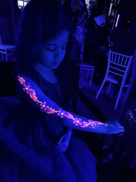 Pinta caritas flúor de flores en el brazo de una niña en una fiesta