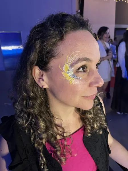 Maquillaje glitter amarillo con plumas en la sien