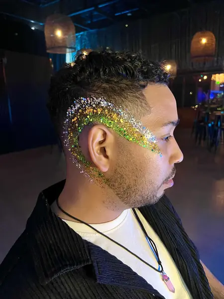Maquillaje glitter dorado y verde en la sien de un hombre