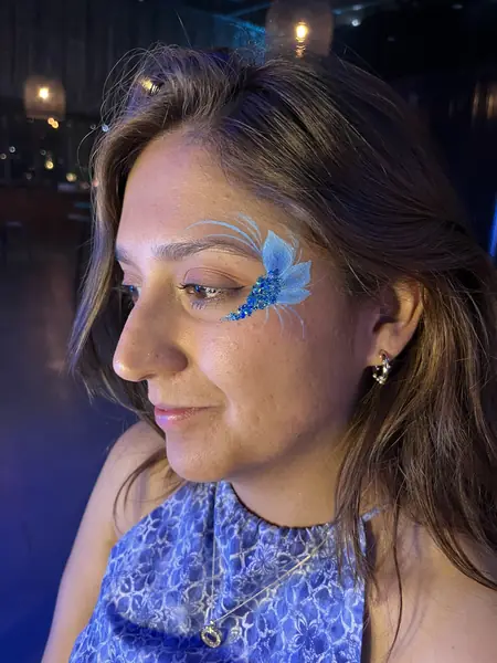 Maquillaje glitter de flor azul en la sien de una mujer