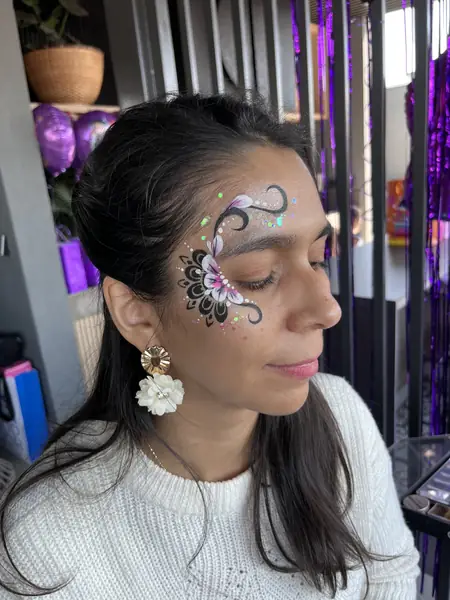 Maquillaje glitter de flor negra y rosada junto al ojo