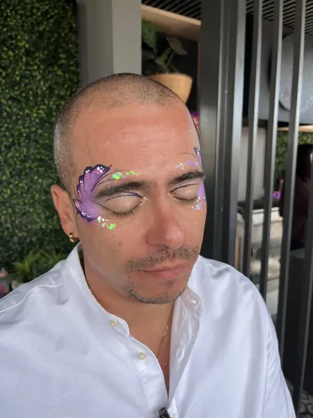Maquillaje glitter de mariposa lila en el ojo de un hombre