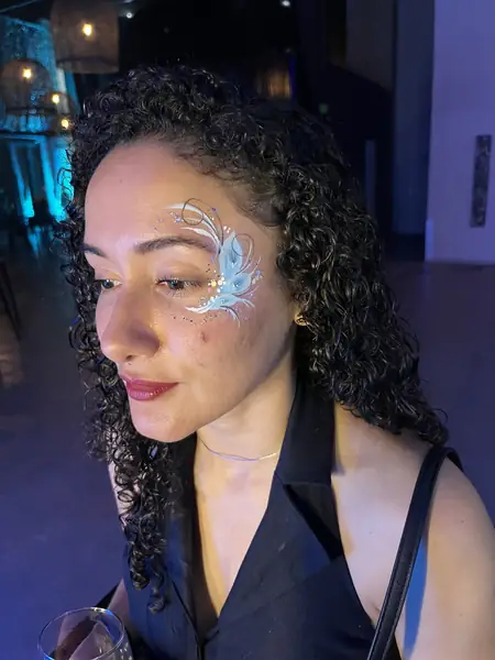 Maquillaje glitter de pluma celeste y blanca junto al ojo