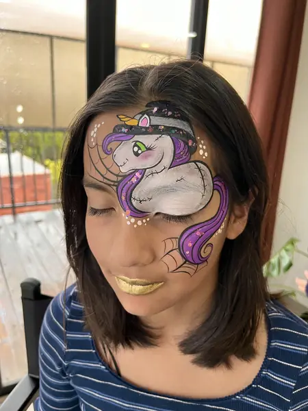 Pinta caritas de unicornio con sombrero de bruja en una niña