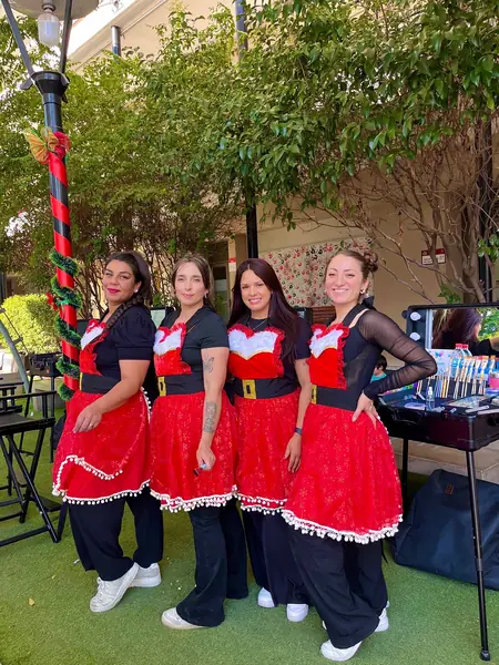Equipo de cuatro maquilladoras de Pinta Caritas Santiago con uniforme navideño junto a su stand en una fiesta de Navidad de empresa
