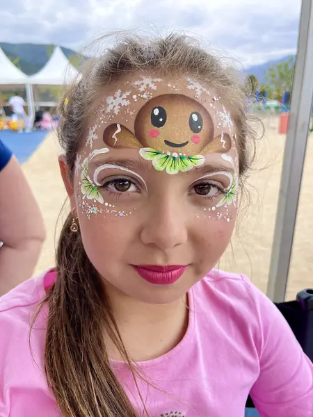 Pinta caritas de galleta de jengibre con copos de nieve en la frente de una niña, fiesta de Navidad