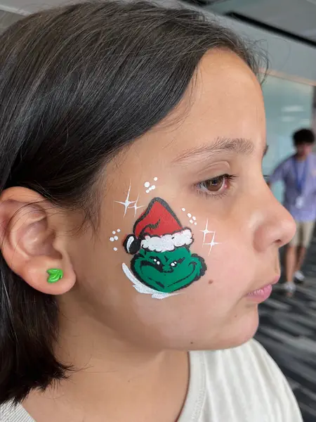 Pinta caritas del Grinch con gorro navideño en la mejilla de una niña